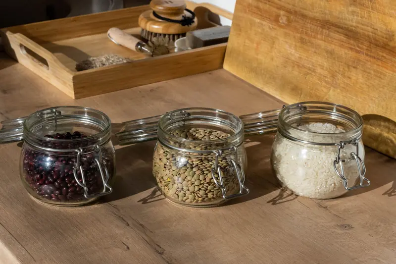 Glass jars of beans, lentils, and uncooked rice on a wooden table with warm lighting