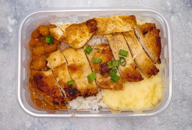 Top view of a tasty home-cooked meal with grilled chicken, beans, and rice in a bento box