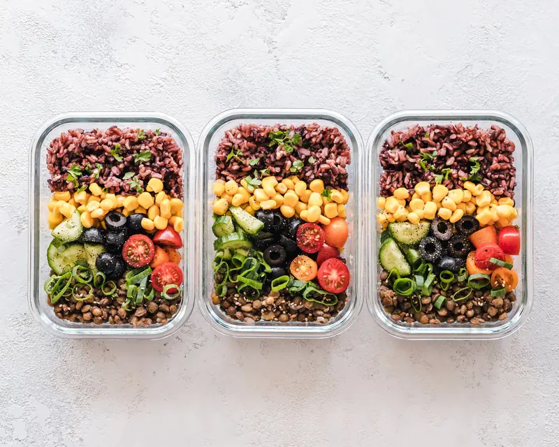 Colorful healthy meal prep with corn, olives, tomatoes, and lentils in glass containers. Perfect for mindful eating