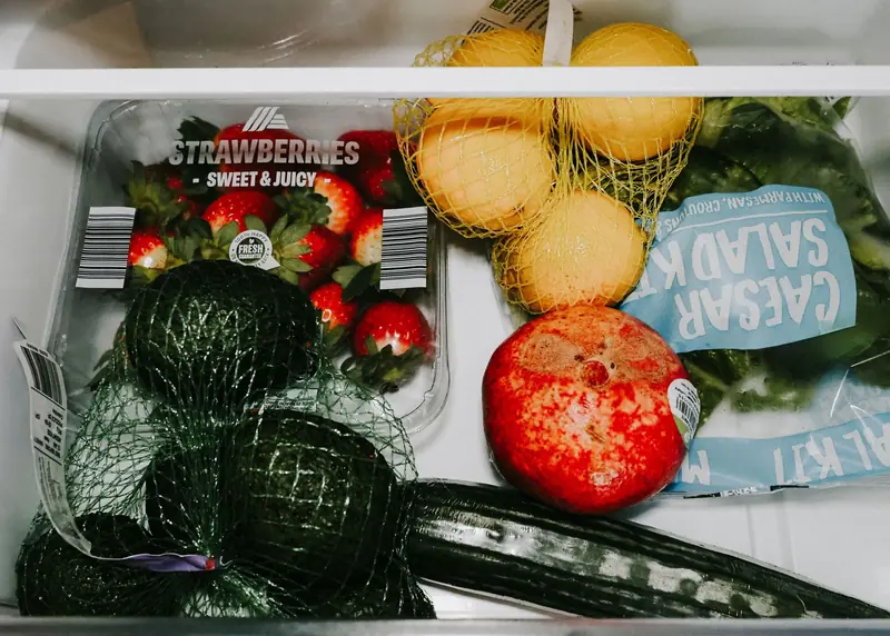 A variety of fresh fruits and vegetables including avocados, lemons, strawberries, and lettuce in a fridge drawer