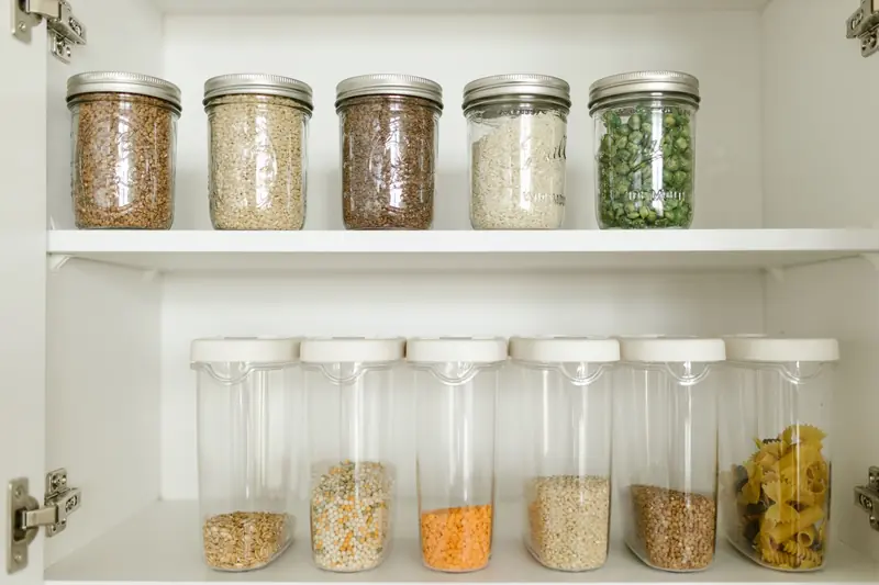 Neatly arranged pantry showcasing grains in glass jars and dry goods in plastic containers