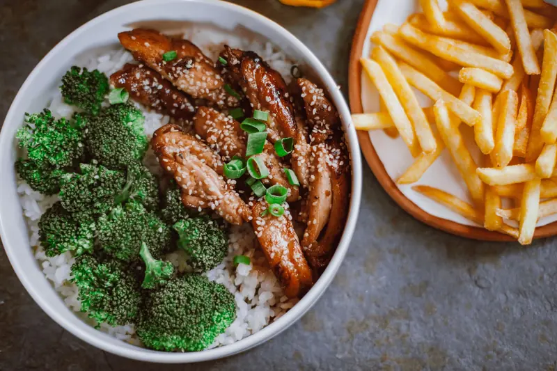 A tasty chicken, broccoli, and rice bowl garnished with sesame seeds, paired with crispy fries