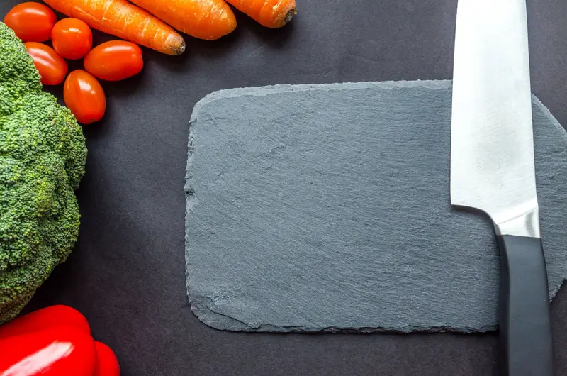 A fresh selection of vegetables including broccoli and carrots with a knife on a slate board