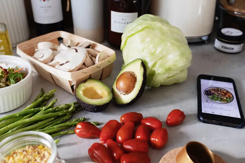 Fresh organic chopped vegetables placed on countertop near kitchen utensils and mobile phone in bright kitchen during preparation salad according to recipe from